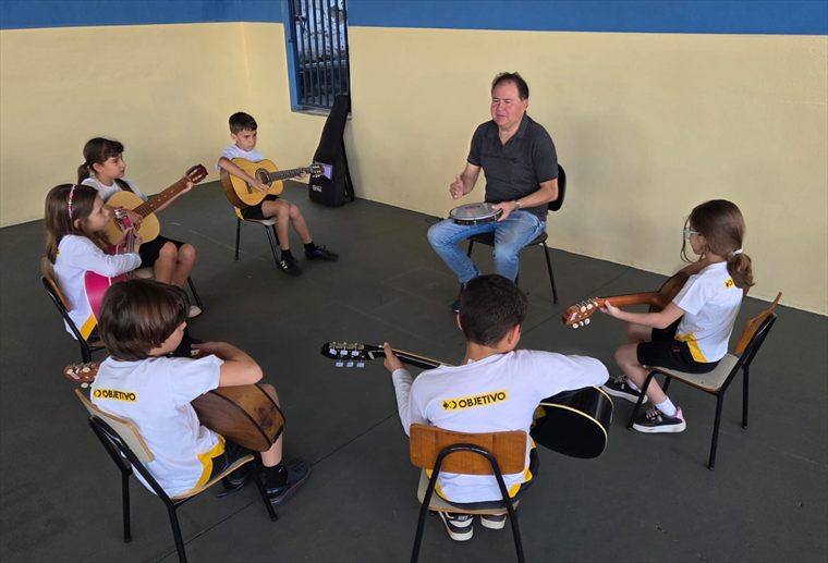 Alunos em roda com violões durante a aula de música, no pátio coberto